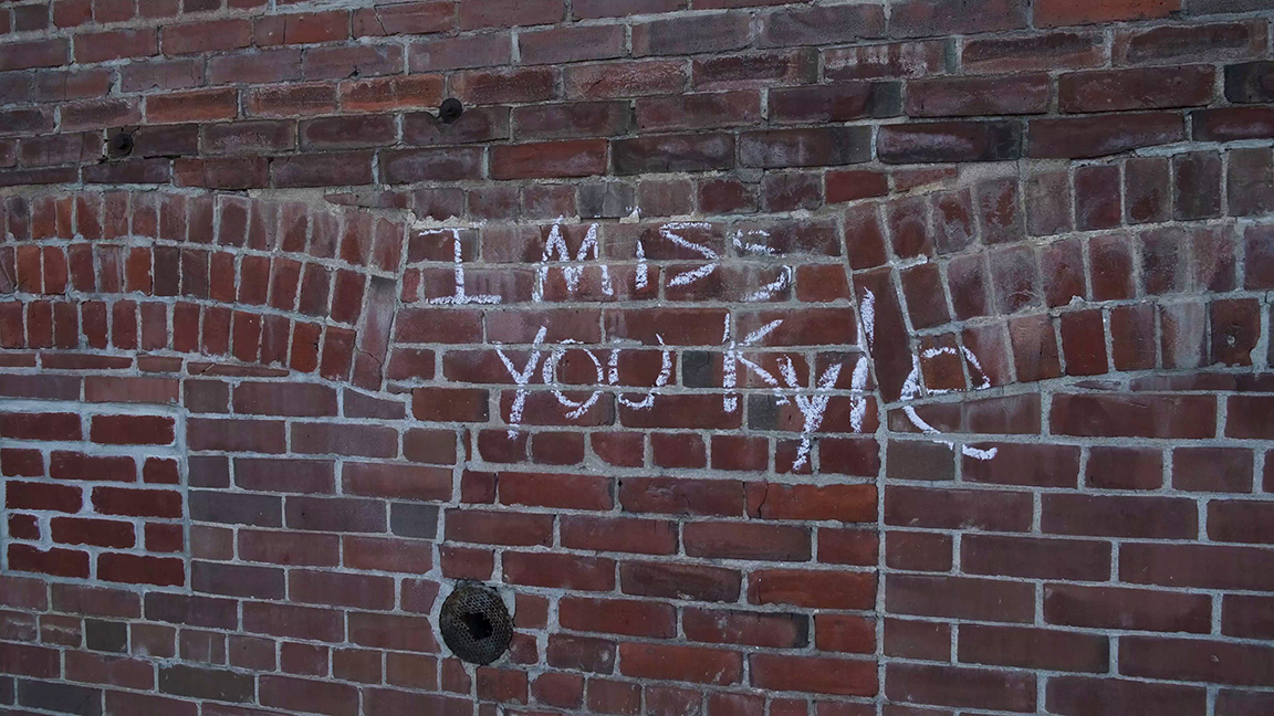 Photo of a brick wall with 'I miss you Kyle' written in chalk, taken by Anne White.